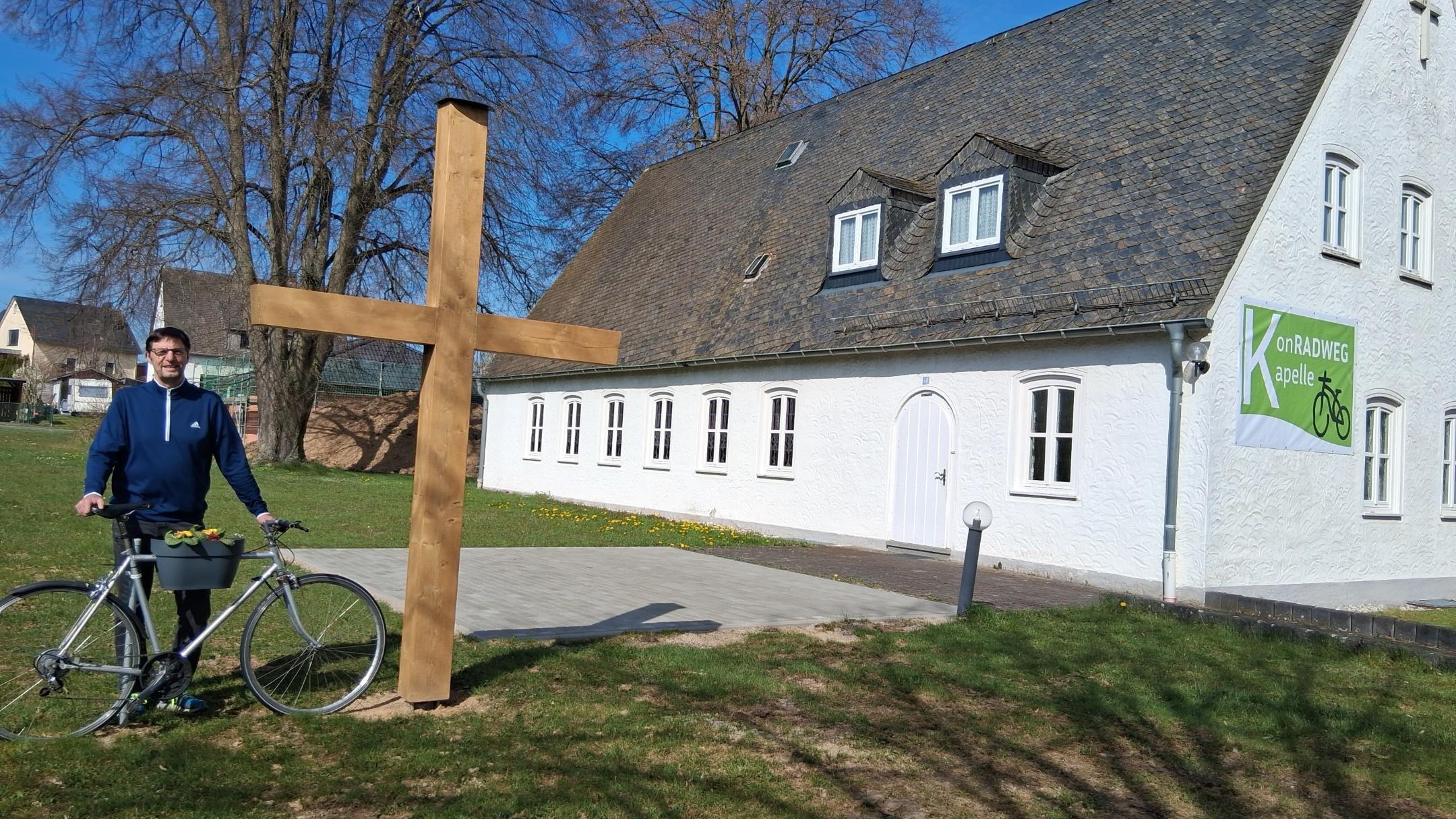 Diakon Franz Jahn mit Fahrrad bei dem neuen Holzkreuz vor der KonRADWEG-Kirche